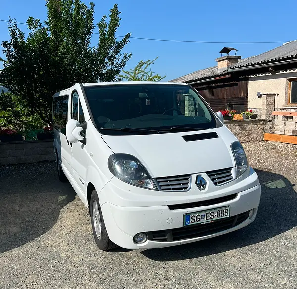 Bel osebni kombi Renault Trafic, primeren za prevoz oseb ali opreme, parkiran na domačem dvorišču.